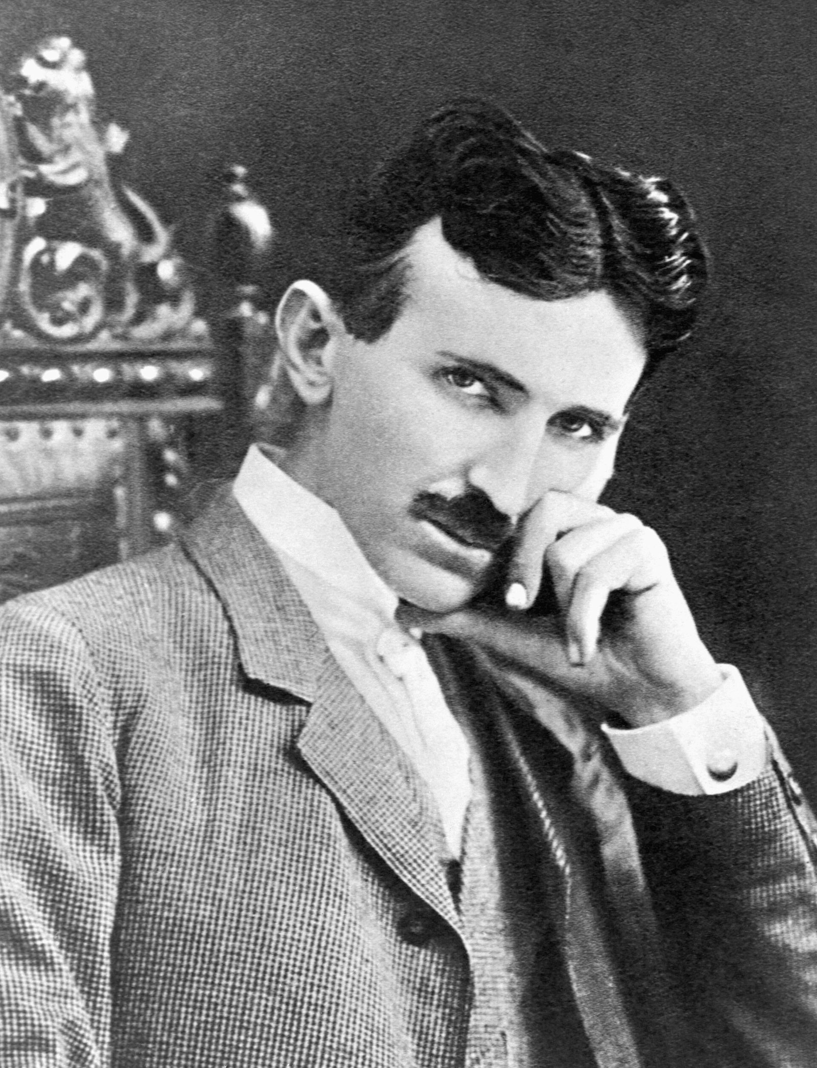 Nikola Tesla seated, about 1896, one hand at his chin